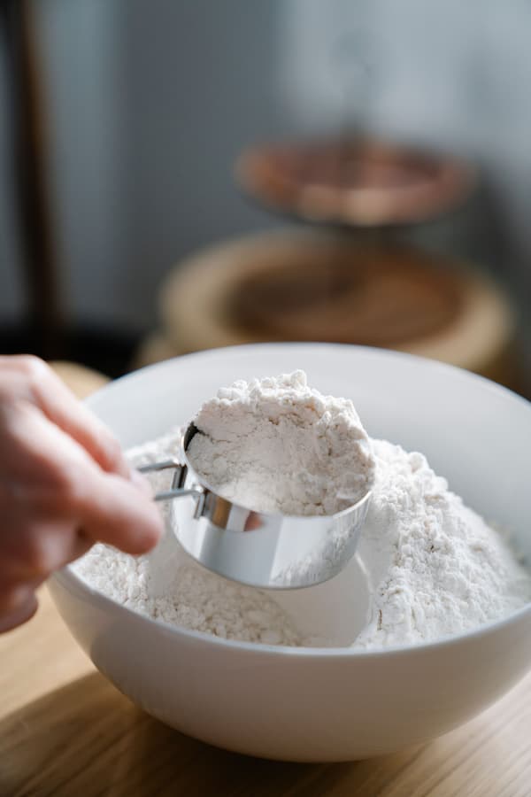 Close-up of a stainless steel measuring cup scooping flour from a white bowl