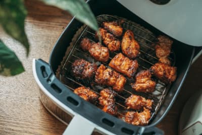 Golden-brown crispy chicken wings cooking inside an air fryer basket on a wire rack.