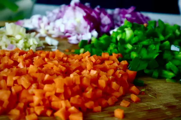 Freshly diced carrots, red onion and green bell pepper on a wooden cutting board